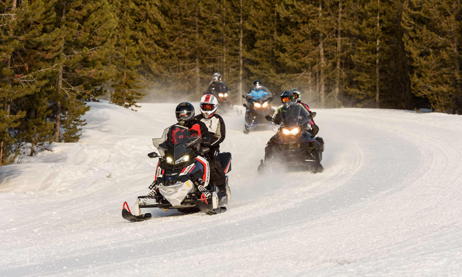 Snowmobiler riding with passenger on trail